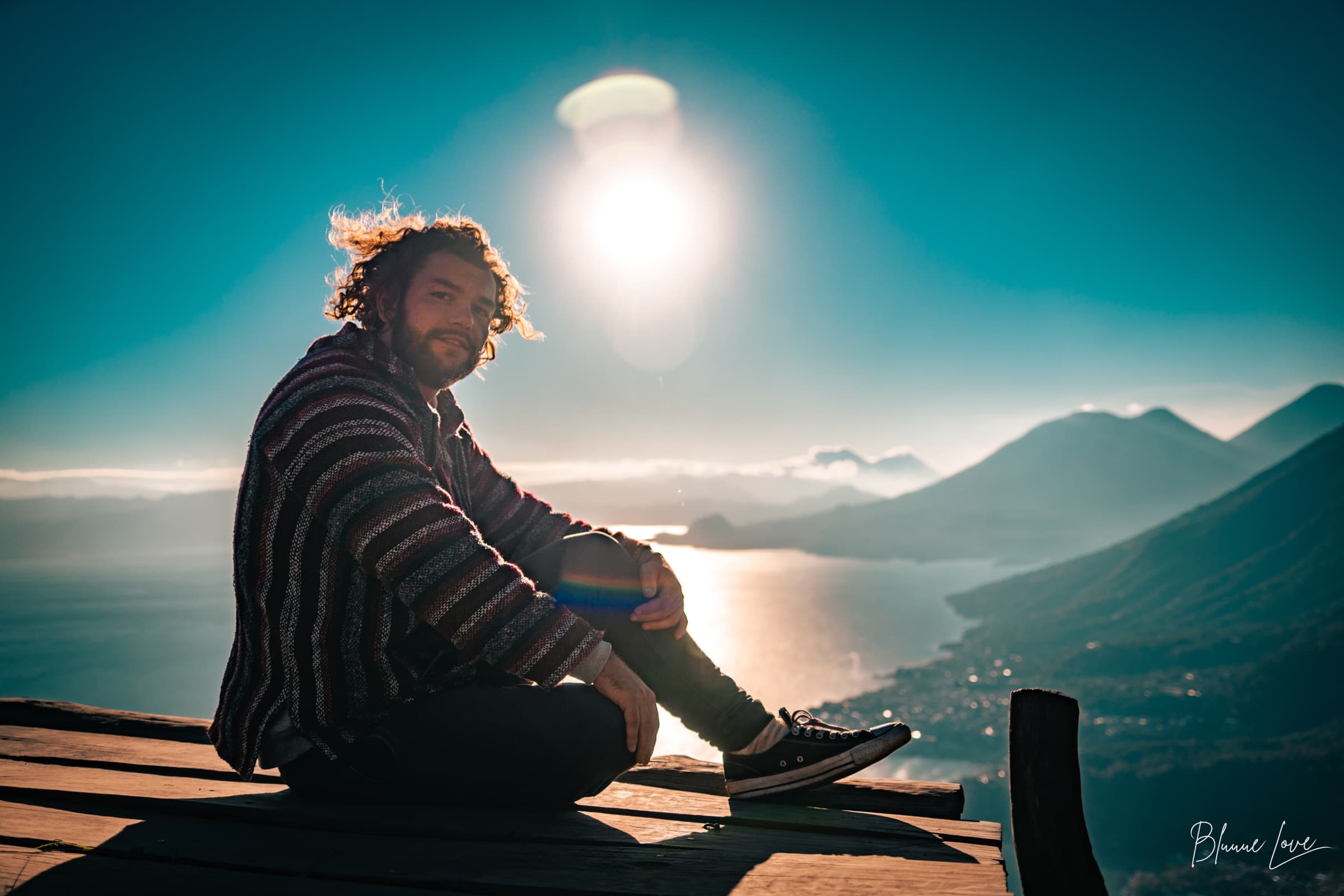 Joshua Sting sitting cross-legged on a mountain ridge at sunrise, looking toward the camera